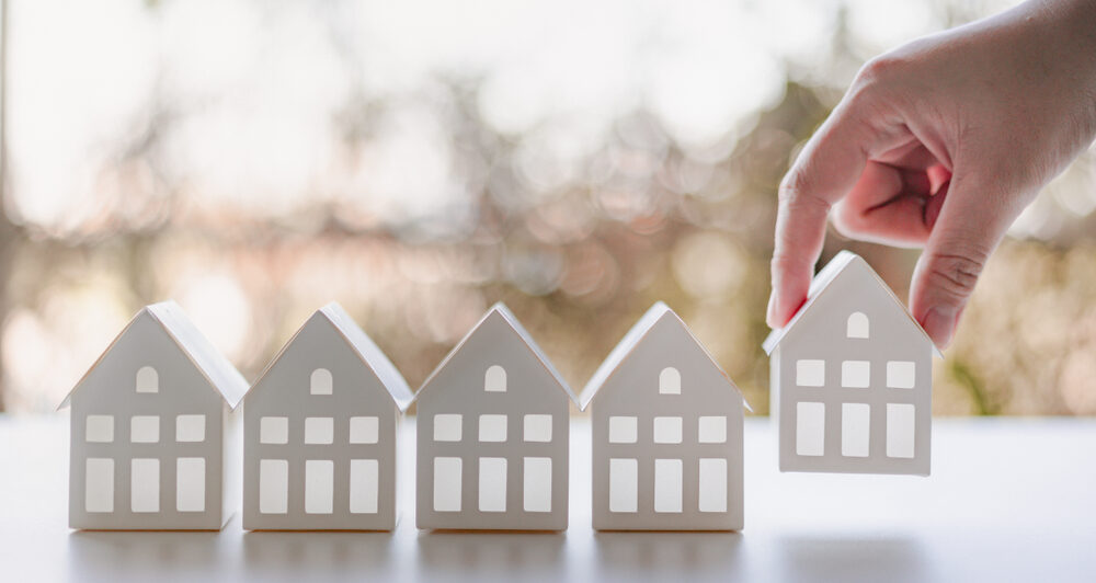 Hand choosing white paper house model from group of houses.