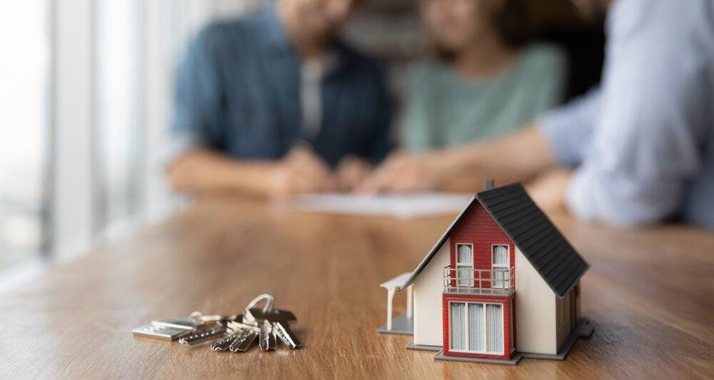 Couple signing a contract in front of model house.